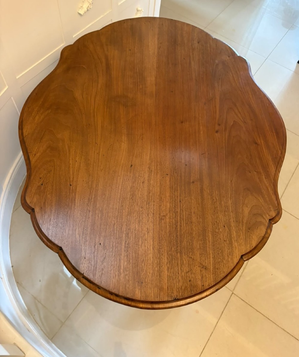 A Victorian figured mahogany tilt-top centre table featuring a shaped serpentine top positioned vertically on a carved central pedestal with four splayed legs. View VII