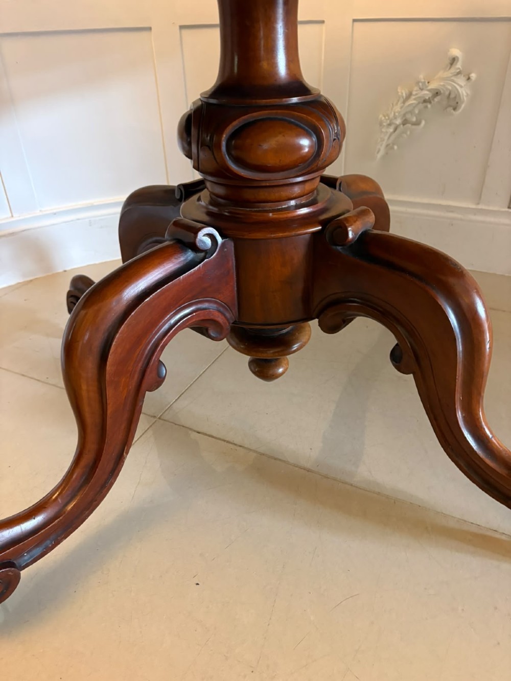 A Victorian figured mahogany tilt-top centre table featuring a shaped serpentine top positioned vertically on a carved central pedestal with four splayed legs. View IX
