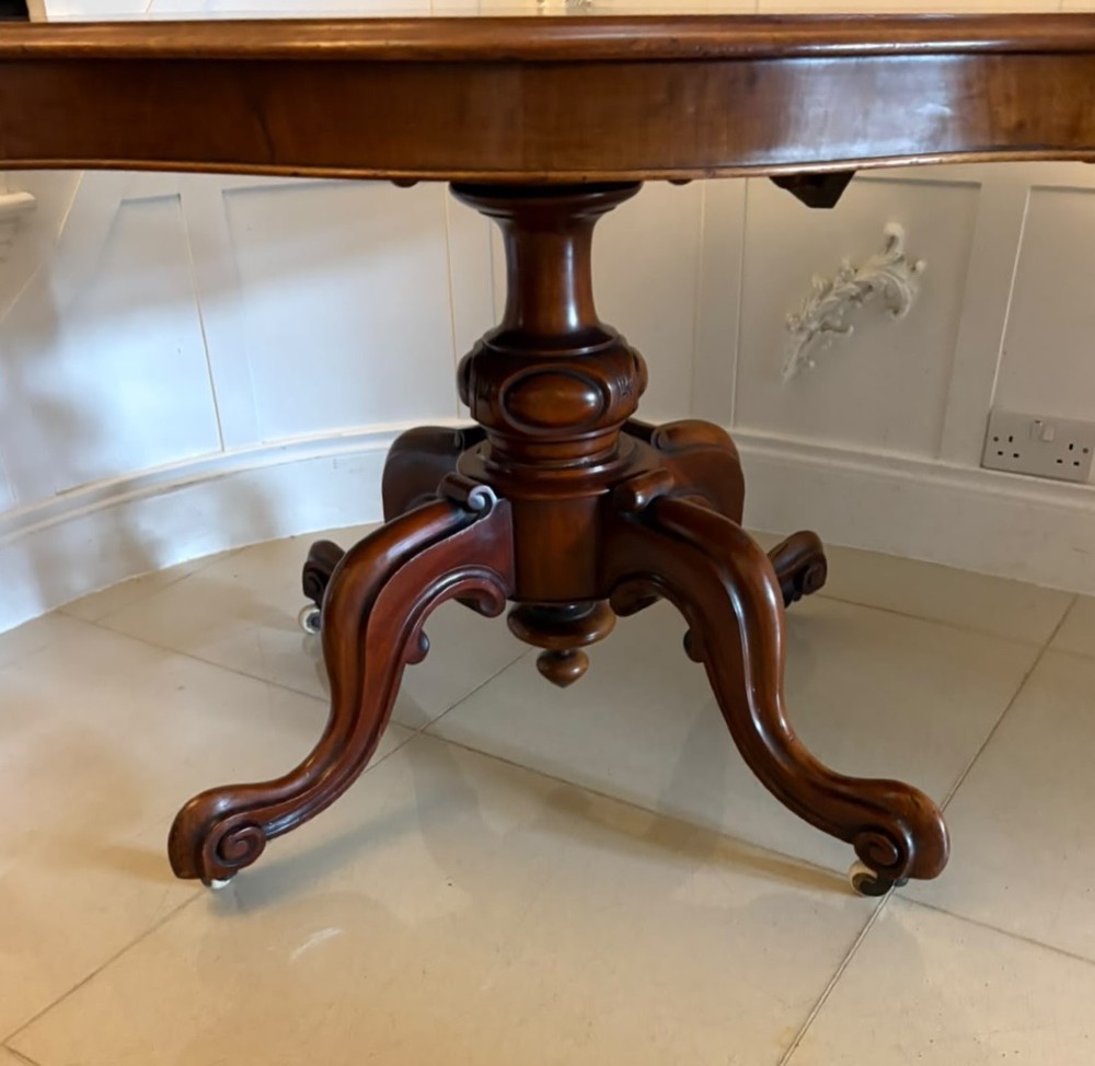 A Victorian figured mahogany tilt-top centre table featuring a shaped serpentine top positioned vertically on a carved central pedestal with four splayed legs. View XI