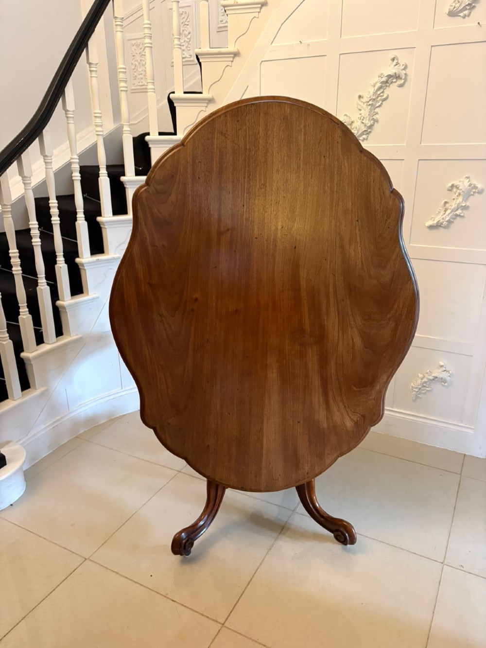 A Victorian figured mahogany tilt-top centre table featuring a shaped serpentine top positioned vertically on a carved central pedestal with four splayed legs.