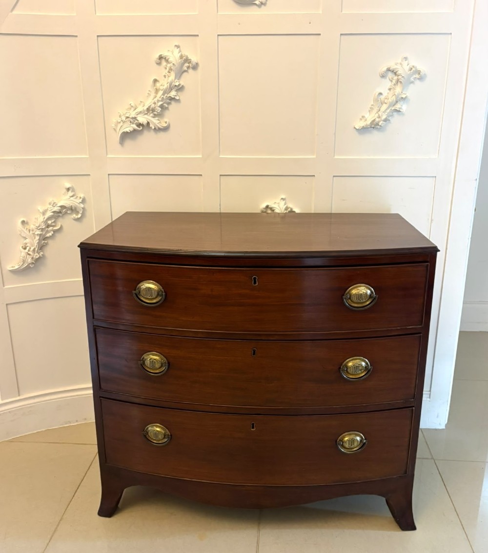 An antique Georgian mahogany bow-front chest featuring three graduating drawers with brass oval handles, supported on splayed feet. View IX