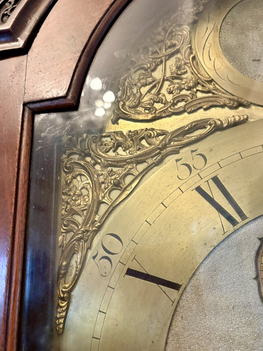 An antique Georgian longcase grandfather clock crafted from flame mahogany wood with an arched brass dial and brass finials. View X