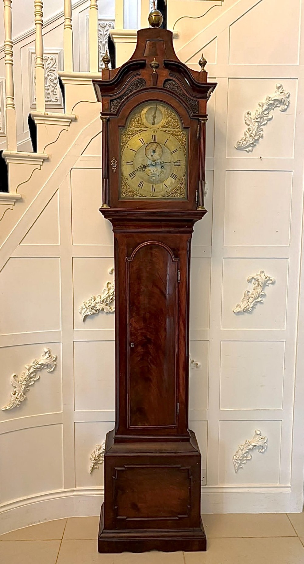 An antique Georgian longcase grandfather clock crafted from flame mahogany wood with an arched brass dial and brass finials. View XV