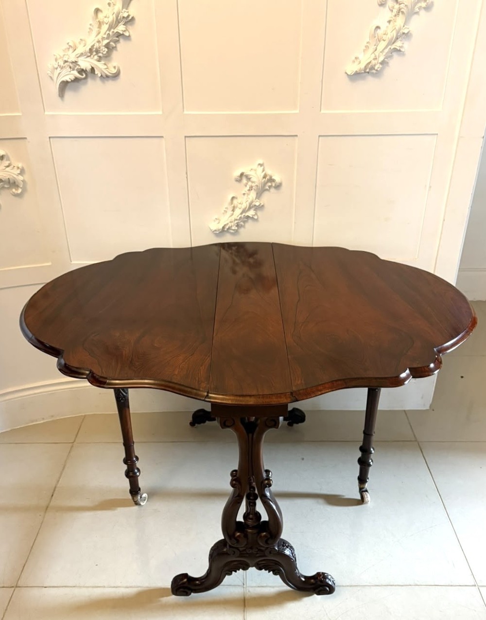 An antique Victorian rosewood Sutherland table with drop leaves, carved legs, and brass castors. View VIII