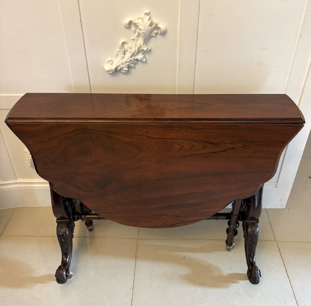 An antique Victorian rosewood Sutherland table with drop leaves, carved legs, and brass castors.