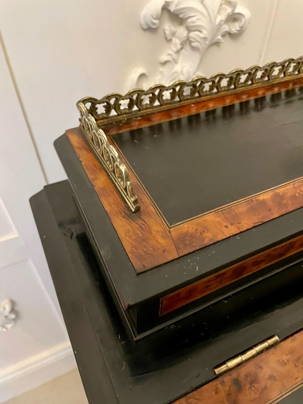 A Victorian ebonised davenport desk featuring walnut crossbanding, a sloped green leather writing surface, side drawers, and a top brass gallery rail. View VI