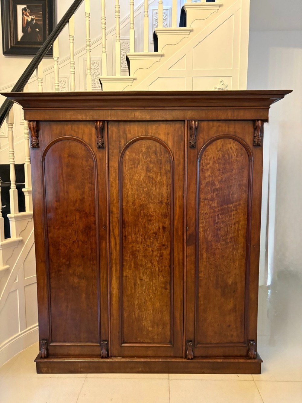A Victorian three-door wardrobe crafted from figured mahogany with arched door panels, carved top corbels, and a wide moulded cornice. View II