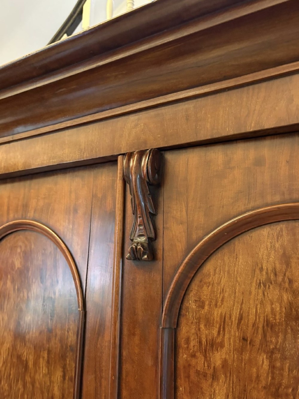 A Victorian three-door wardrobe crafted from figured mahogany with arched door panels, carved top corbels, and a wide moulded cornice. View V