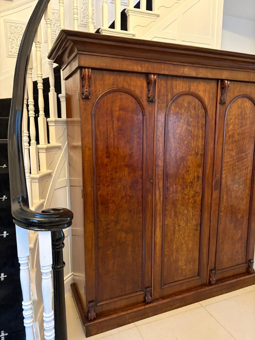 A Victorian three-door wardrobe crafted from figured mahogany with arched door panels, carved top corbels, and a wide moulded cornice. View XII