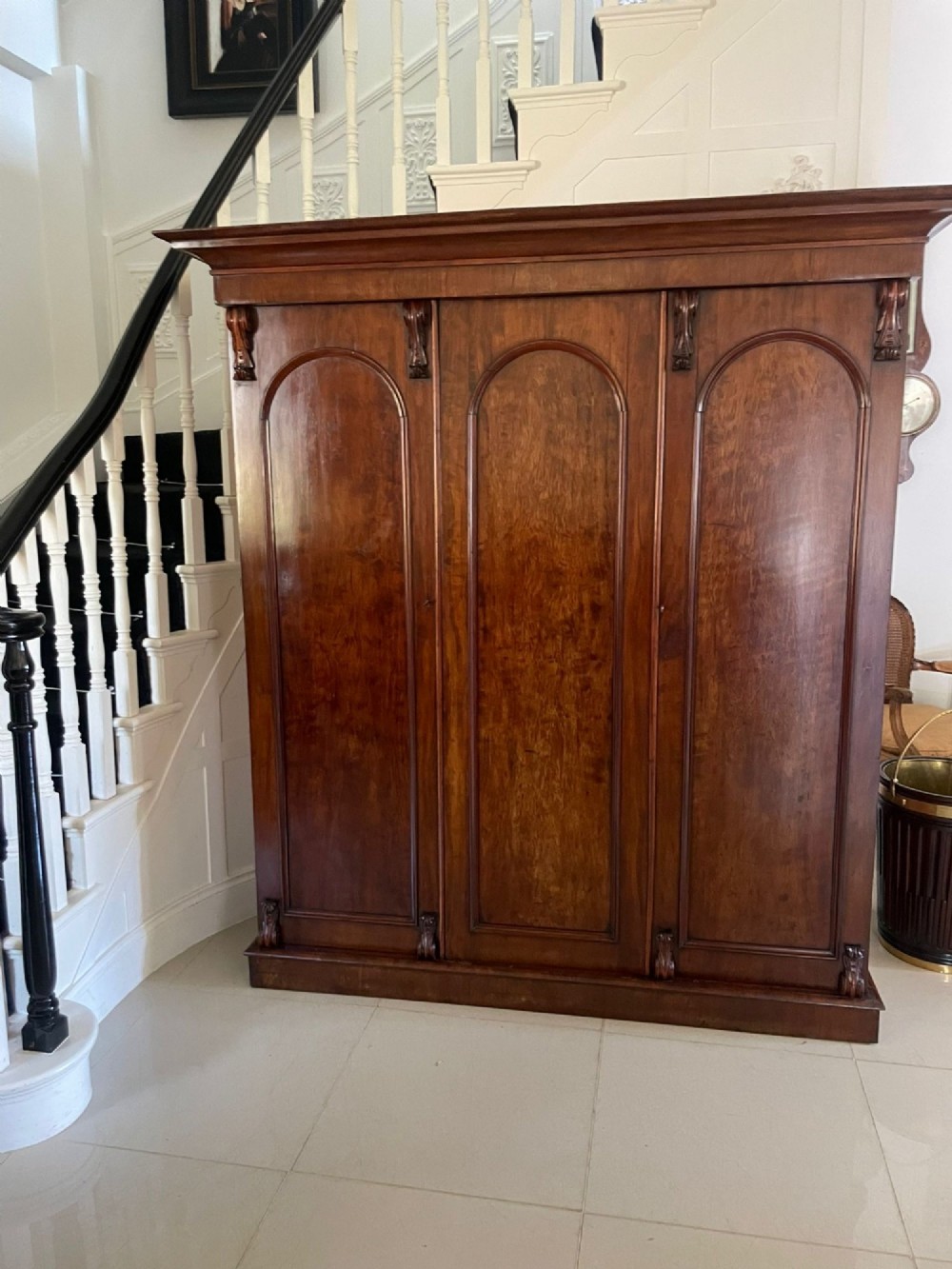 A Victorian three-door wardrobe crafted from figured mahogany with arched door panels, carved top corbels, and a wide moulded cornice. View XIV