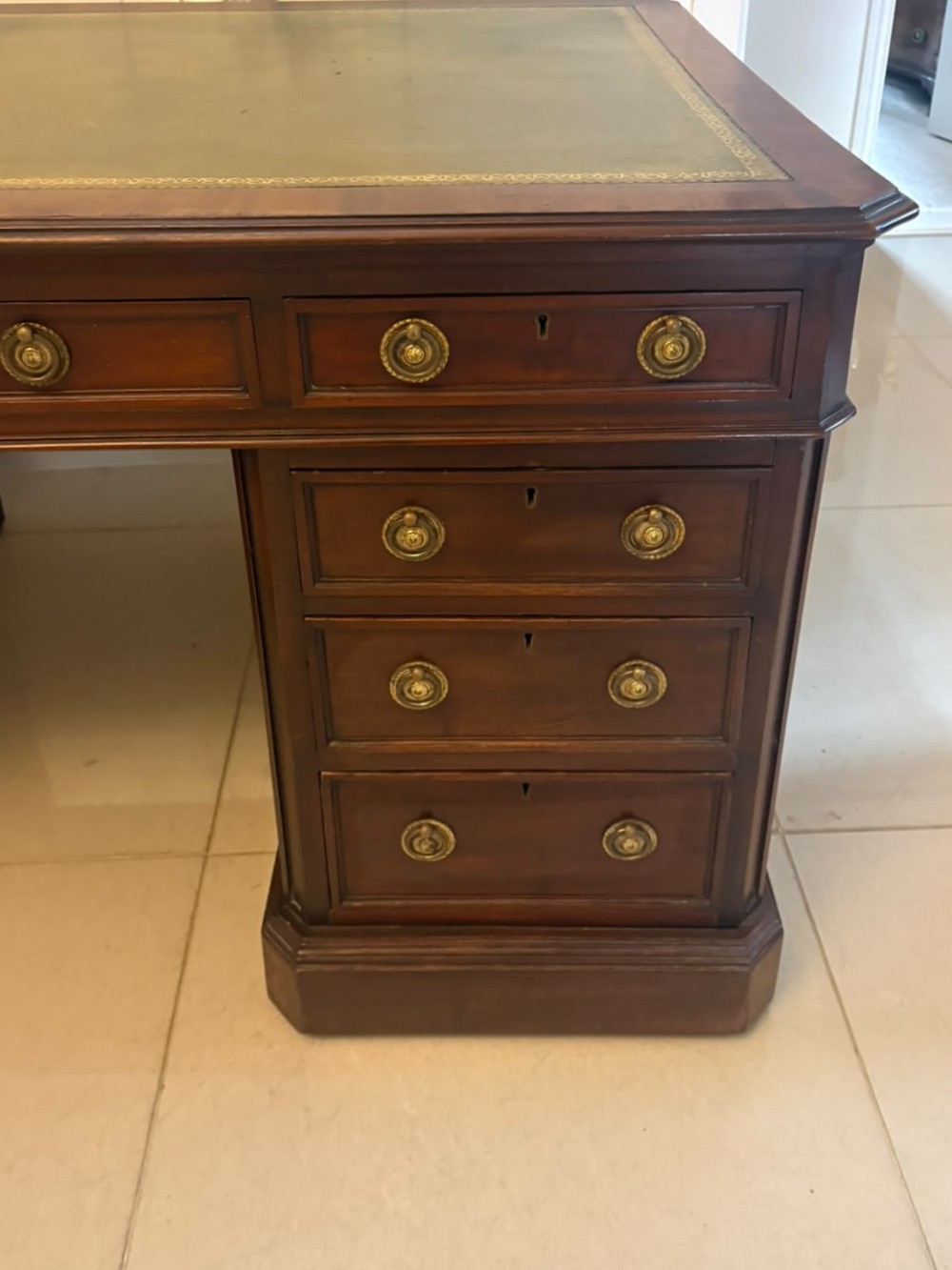 A Victorian mahogany pedestal desk featuring a green leather inset writing surface, nine drawers with brass ring pulls, and a plinth base. View V