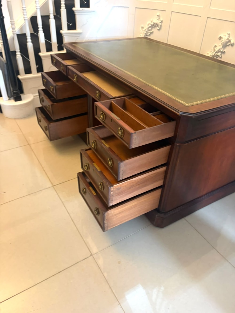 A Victorian mahogany pedestal desk featuring a green leather inset writing surface, nine drawers with brass ring pulls, and a plinth base. View XIV