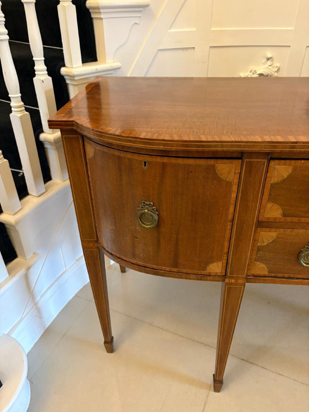 An Edwardian mahogany sideboard featuring satinwood crossbanded inlay, central drawers, flanking curved cupboards, brass ring handles, and square tapered legs. View II