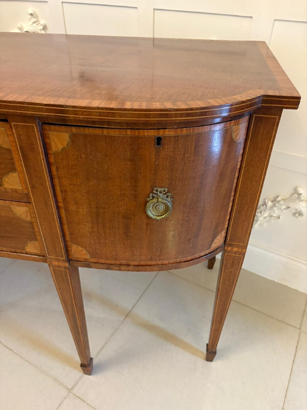 An Edwardian mahogany sideboard featuring satinwood crossbanded inlay, central drawers, flanking curved cupboards, brass ring handles, and square tapered legs. View VI