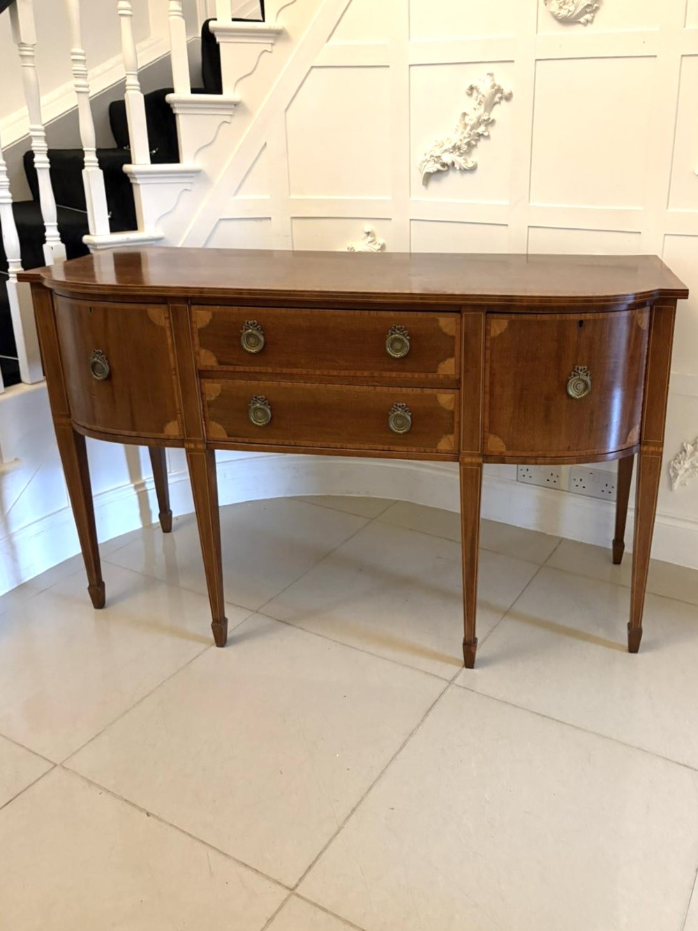 An Edwardian mahogany sideboard featuring satinwood crossbanded inlay, central drawers, flanking curved cupboards, brass ring handles, and square tapered legs. View X