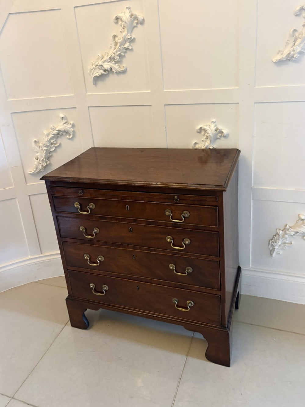 A small Georgian mahogany chest of drawers featuring four graduated drawers with brass swan-neck handles, a pull-out brushing slide, and bracket feet. View IV