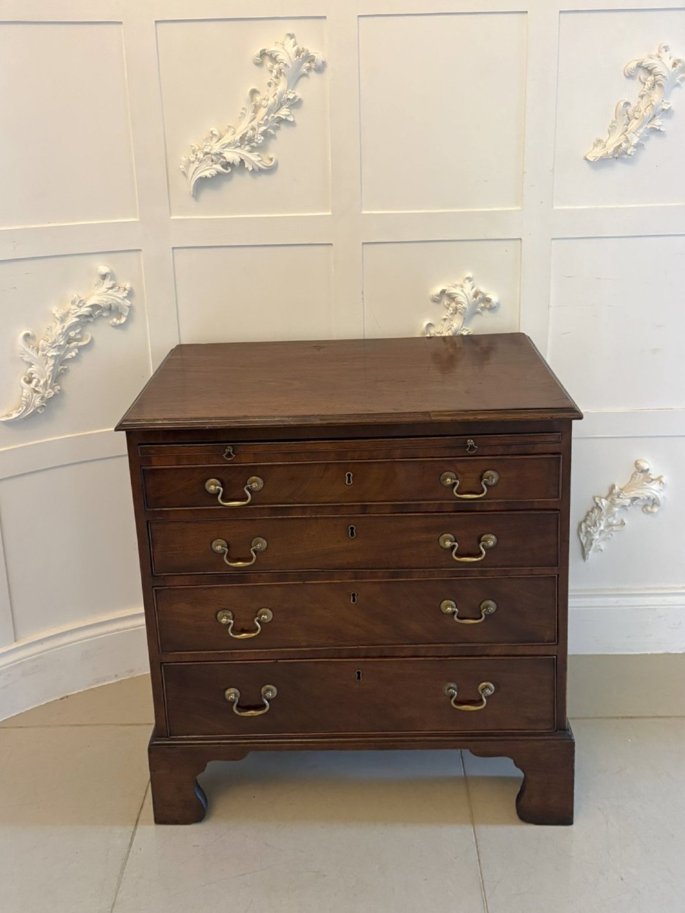 A small Georgian mahogany chest of drawers featuring four graduated drawers with brass swan-neck handles, a pull-out brushing slide, and bracket feet.