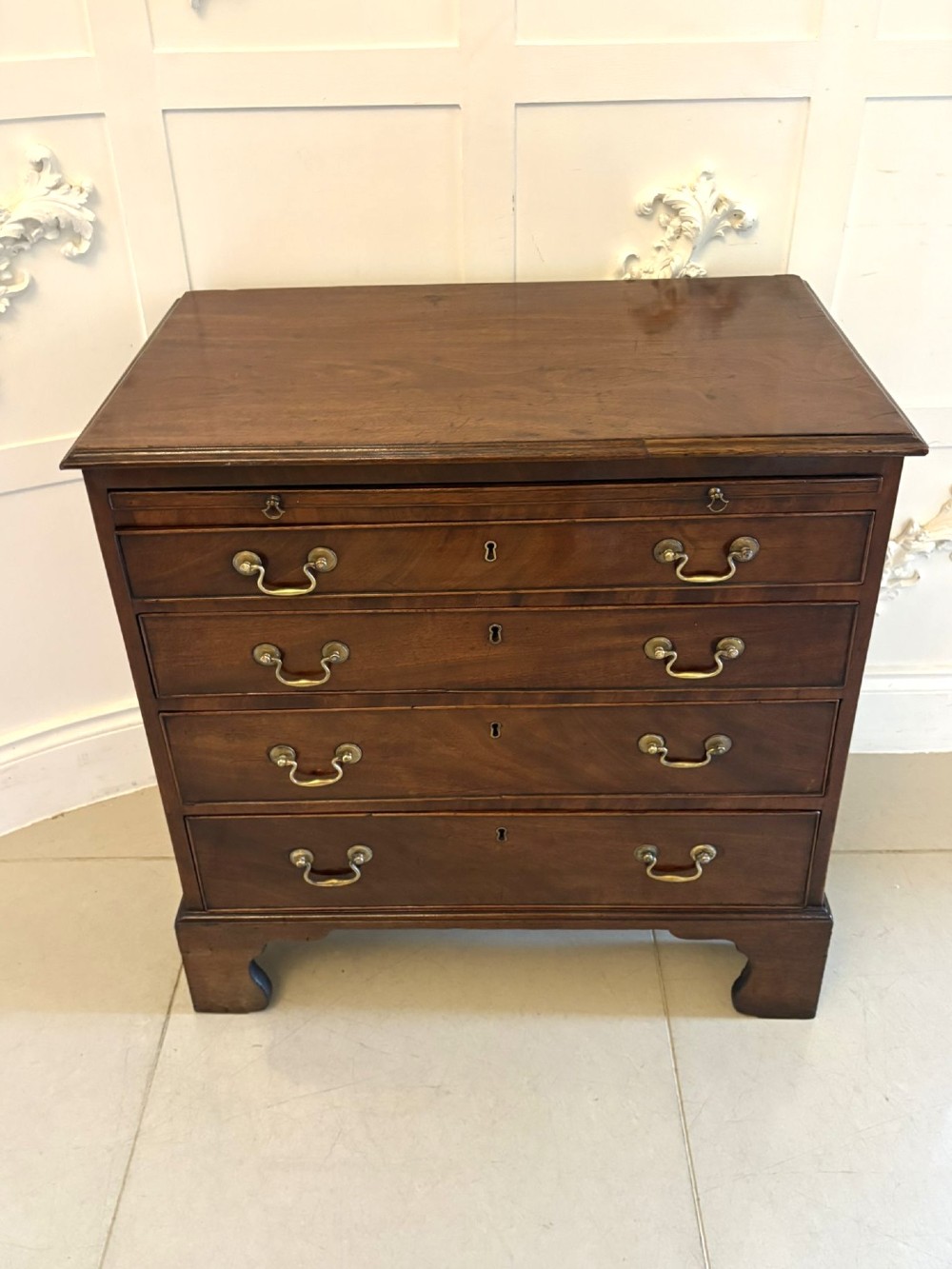 A small Georgian mahogany chest of drawers featuring four graduated drawers with brass swan-neck handles, a pull-out brushing slide, and bracket feet. View V