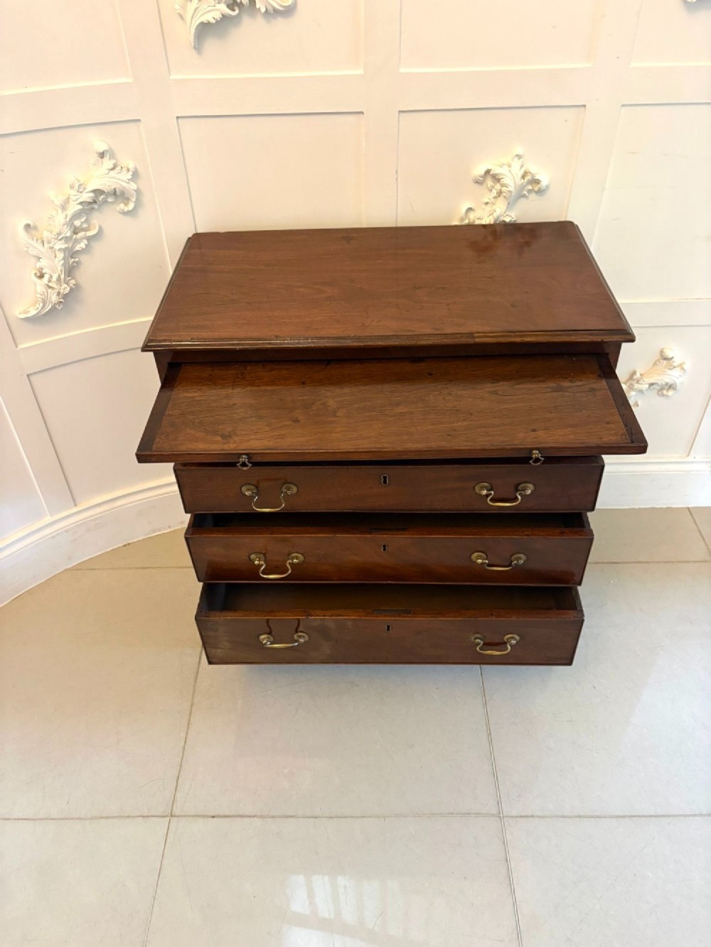 A small Georgian mahogany chest of drawers featuring four graduated drawers with brass swan-neck handles, a pull-out brushing slide, and bracket feet. View VI