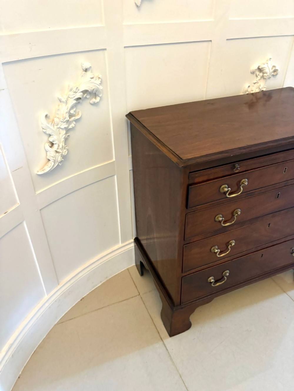 A small Georgian mahogany chest of drawers featuring four graduated drawers with brass swan-neck handles, a pull-out brushing slide, and bracket feet. View IX