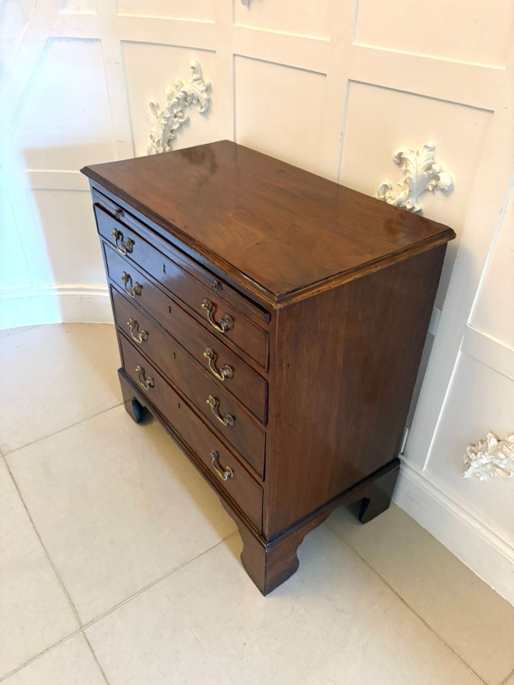 A small Georgian mahogany chest of drawers featuring four graduated drawers with brass swan-neck handles, a pull-out brushing slide, and bracket feet. View X