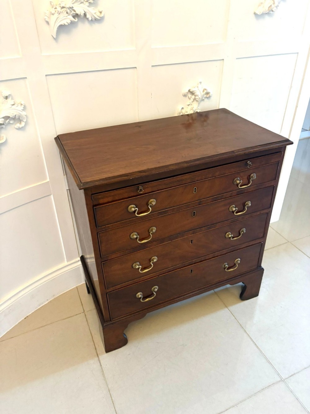 A small Georgian mahogany chest of drawers featuring four graduated drawers with brass swan-neck handles, a pull-out brushing slide, and bracket feet. View XI