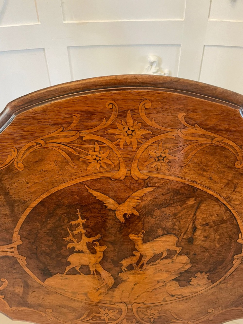 An antique walnut tilt-top side table featuring an oval top with elaborate marquetry depicting alpine wildlife and a carved tripod pedestal base. View II
