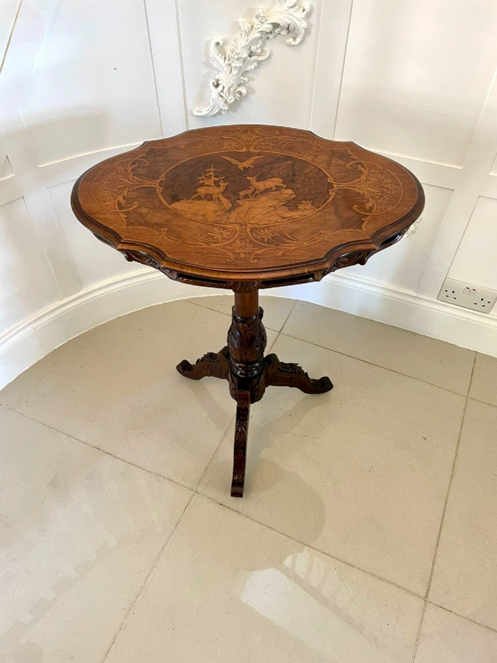 An antique walnut tilt-top side table featuring an oval top with elaborate marquetry depicting alpine wildlife and a carved tripod pedestal base. View X