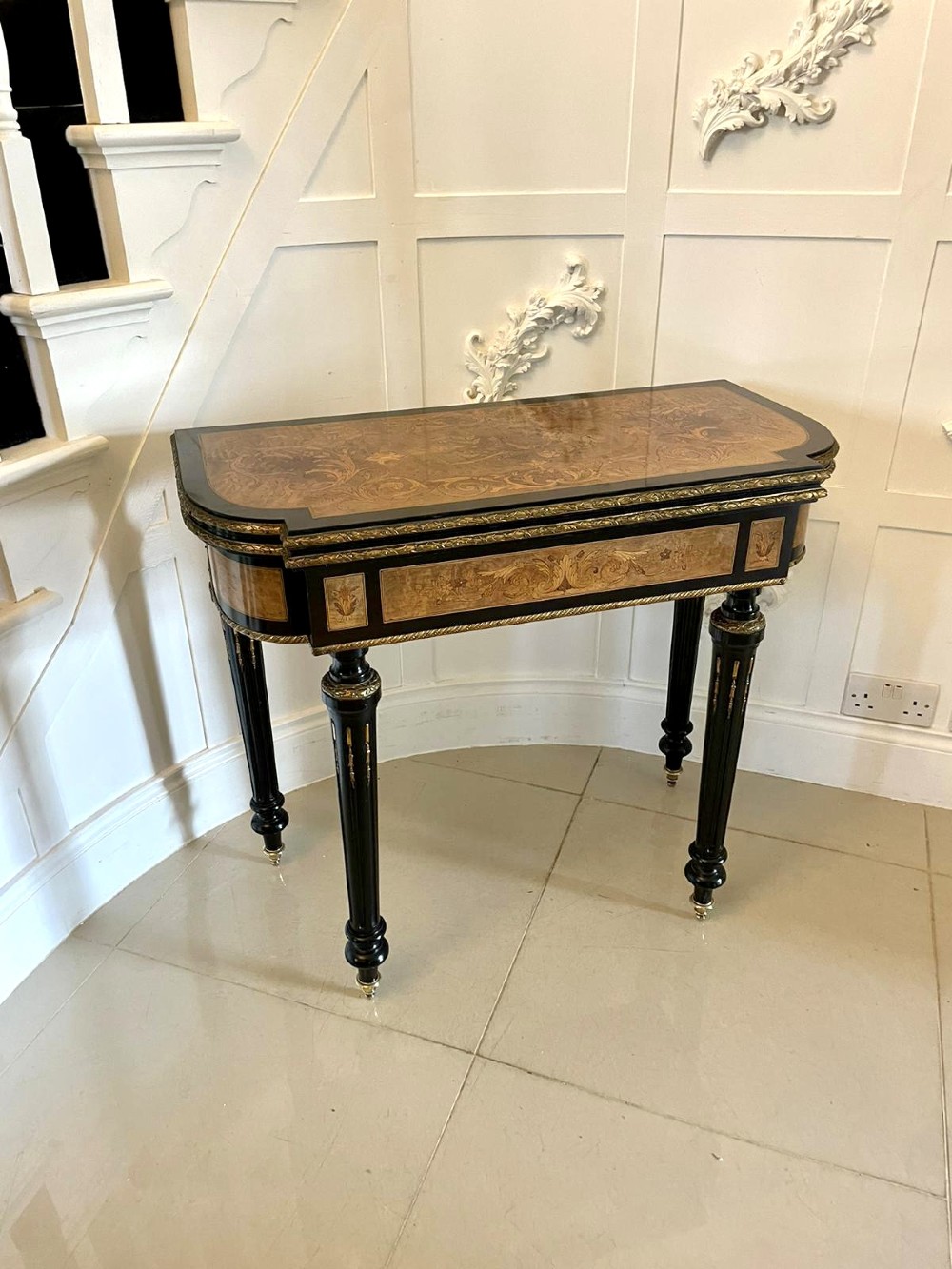 An antique French ebonised and walnut marquetry fold-over card table with gilt bronze mounts and fluted legs.