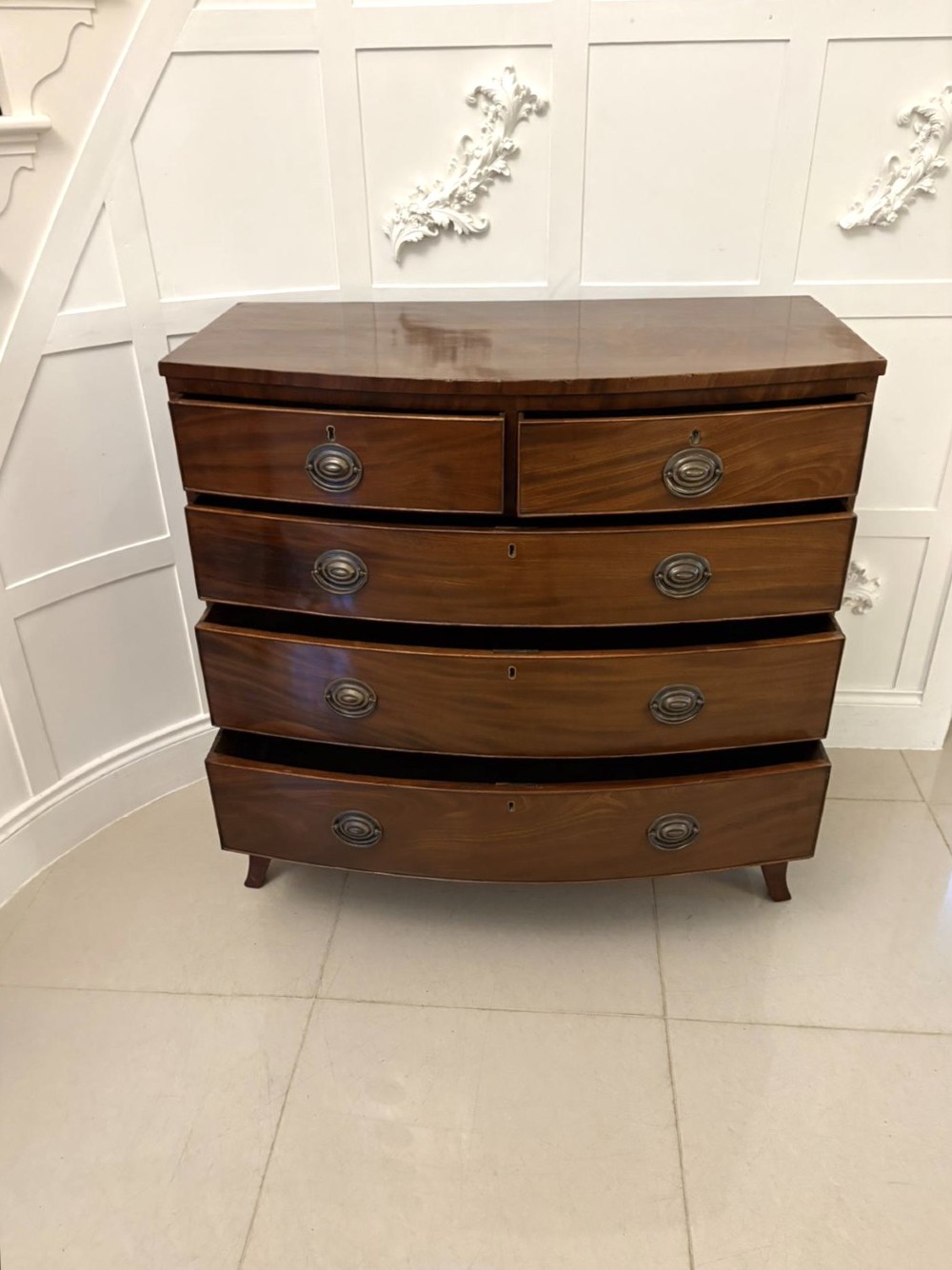A George III mahogany bow-fronted chest featuring two short over three long graduating drawers with brass oval handles and splayed bracket feet. View II