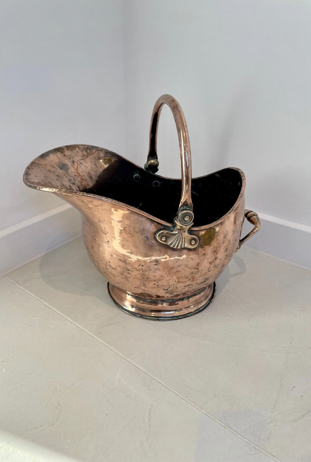 An antique George III copper helmet-shaped coal scuttle featuring an overhead swing handle, a rear loop handle, and a circular stepped pedestal base.