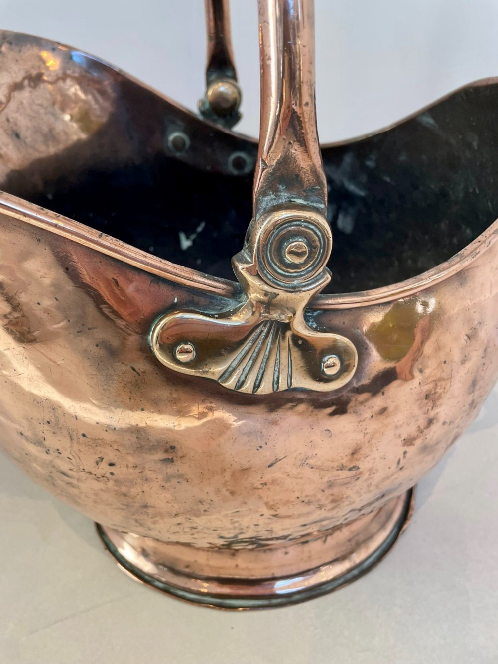 An antique George III copper helmet-shaped coal scuttle featuring an overhead swing handle, a rear loop handle, and a circular stepped pedestal base. View VIII