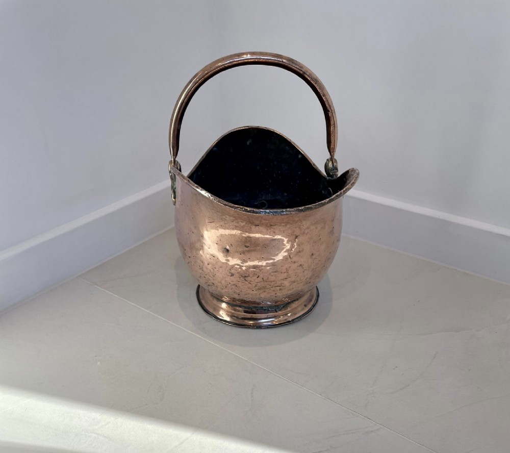 An antique George III copper helmet-shaped coal scuttle featuring an overhead swing handle, a rear loop handle, and a circular stepped pedestal base. View XI