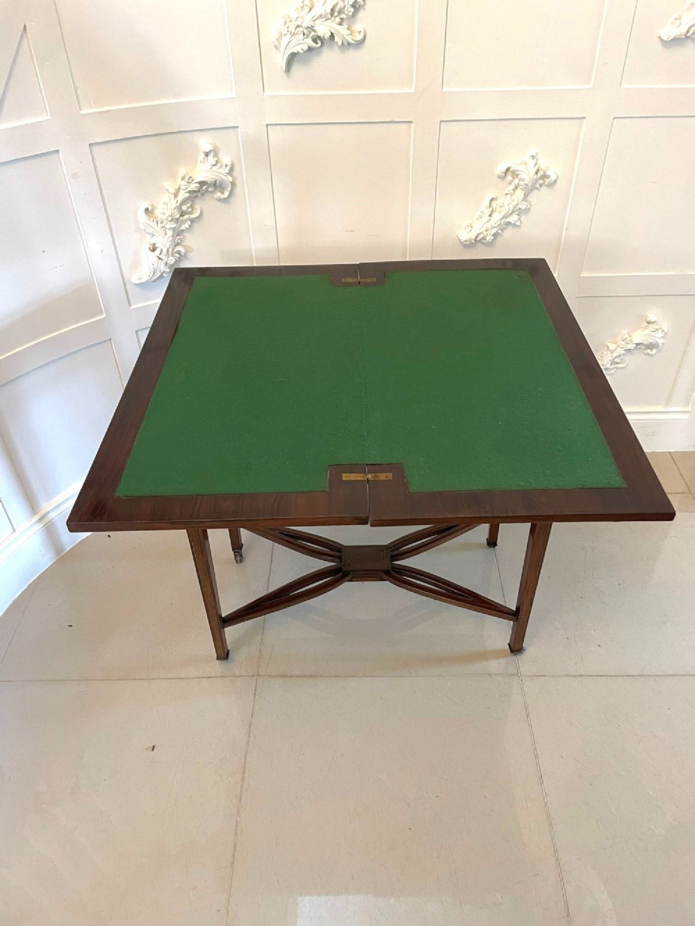An Edwardian dark rosewood folding card table with floral satinwood corner inlays and an X-frame stretcher resting on brass castors. View III