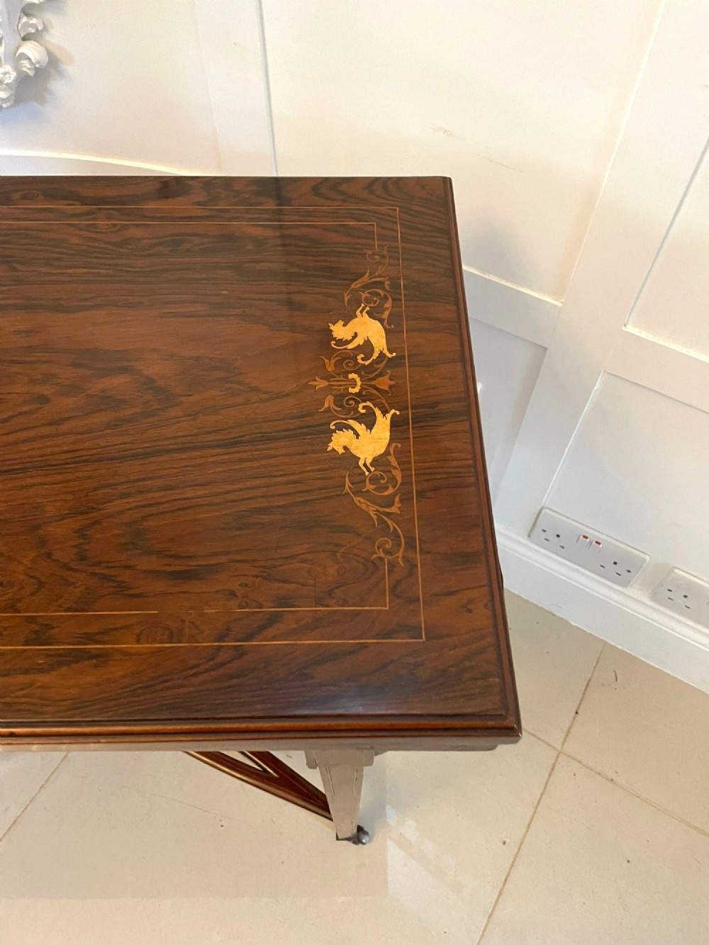 An Edwardian dark rosewood folding card table with floral satinwood corner inlays and an X-frame stretcher resting on brass castors. View V