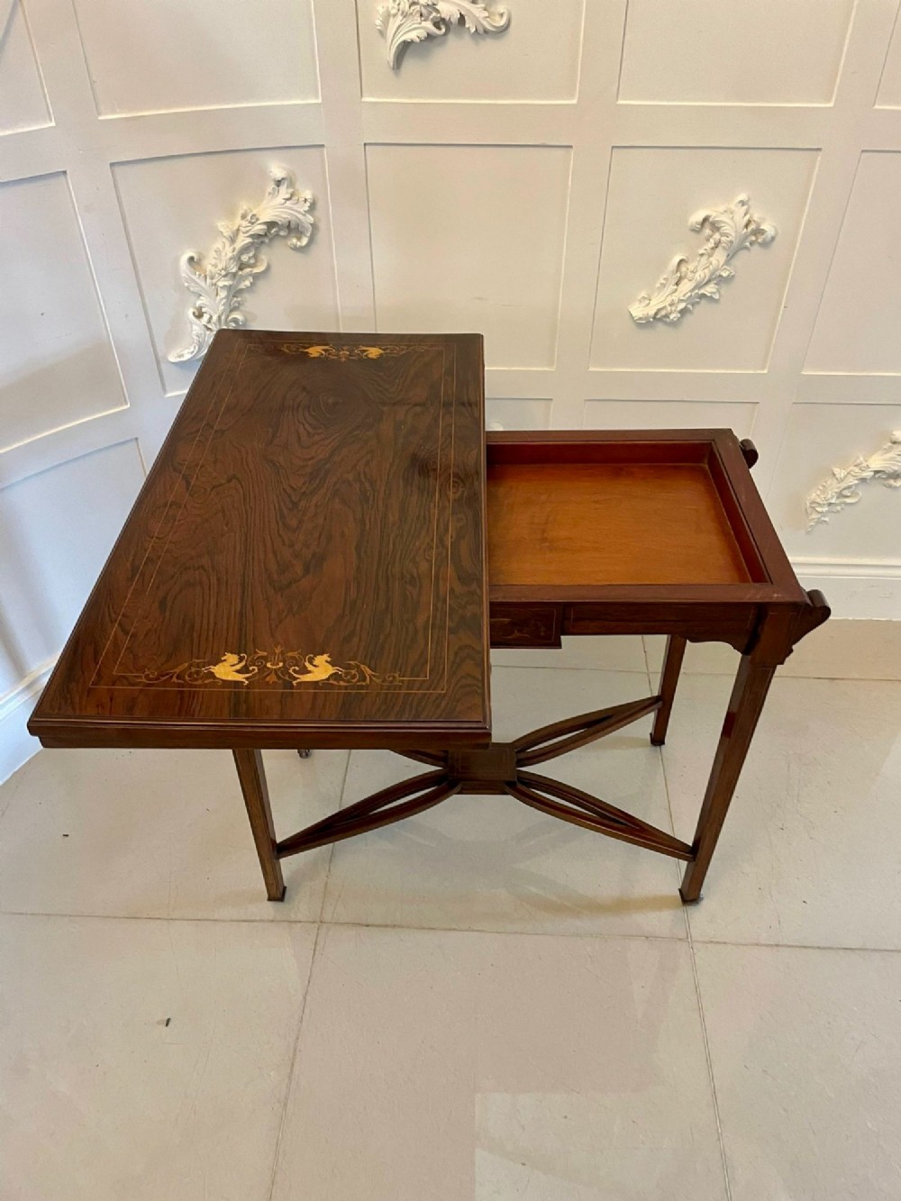 An Edwardian dark rosewood folding card table with floral satinwood corner inlays and an X-frame stretcher resting on brass castors. View VI