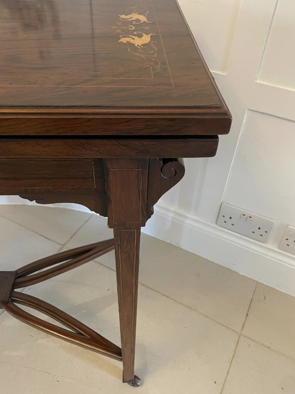 An Edwardian dark rosewood folding card table with floral satinwood corner inlays and an X-frame stretcher resting on brass castors. View VIII