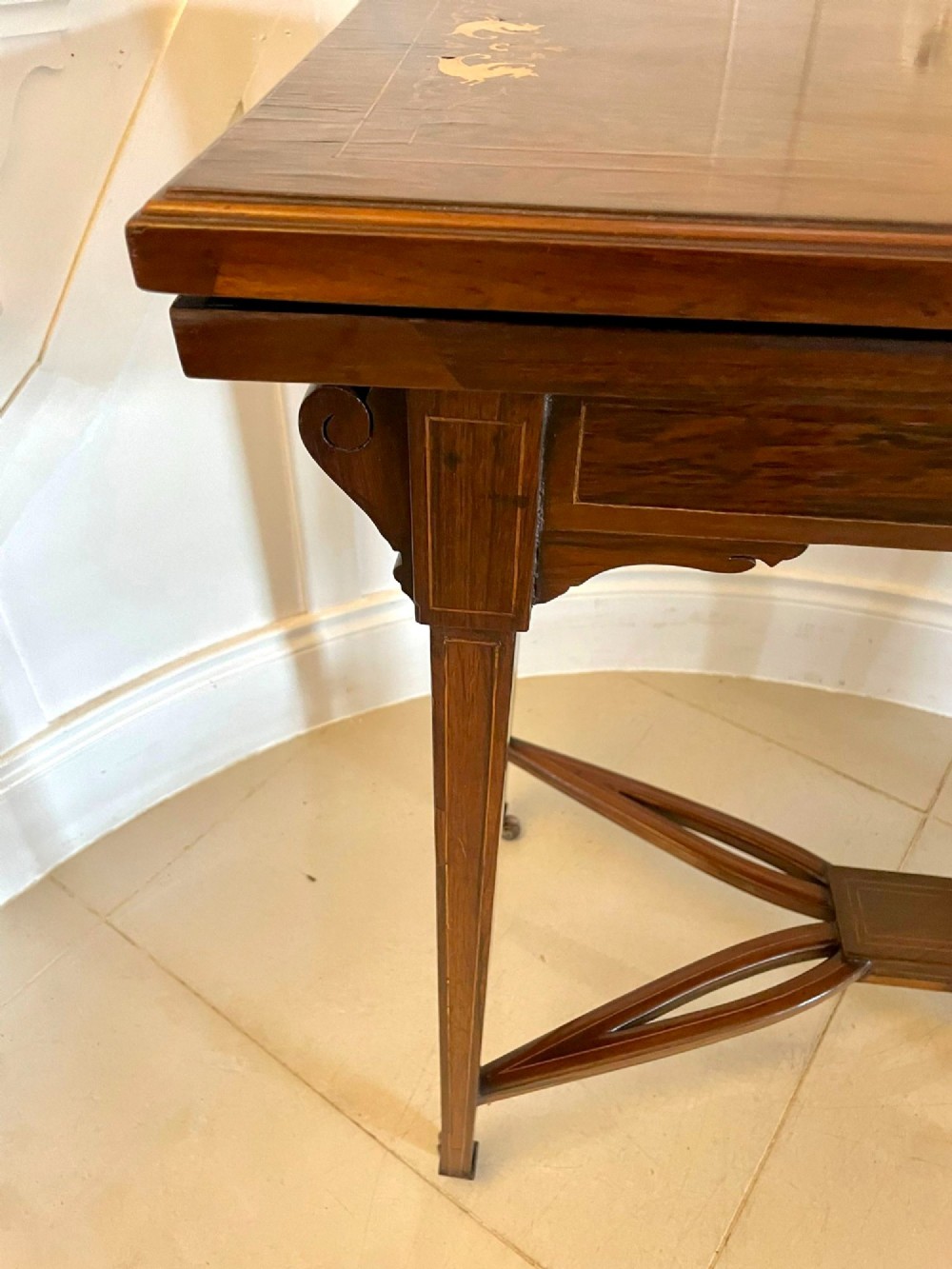 An Edwardian dark rosewood folding card table with floral satinwood corner inlays and an X-frame stretcher resting on brass castors. View IX