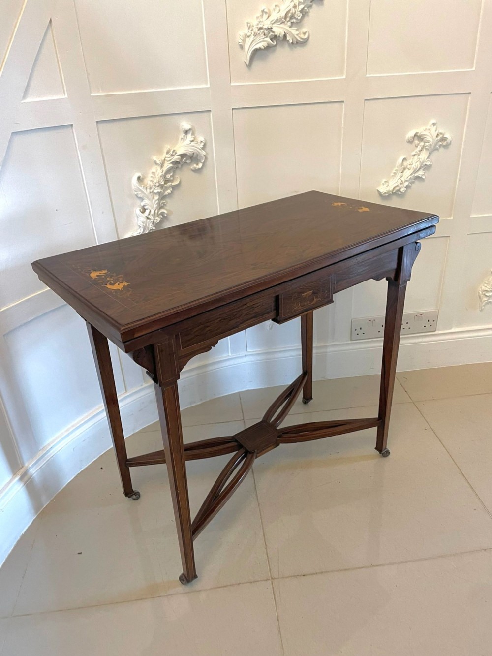 An Edwardian dark rosewood folding card table with floral satinwood corner inlays and an X-frame stretcher resting on brass castors. View XI