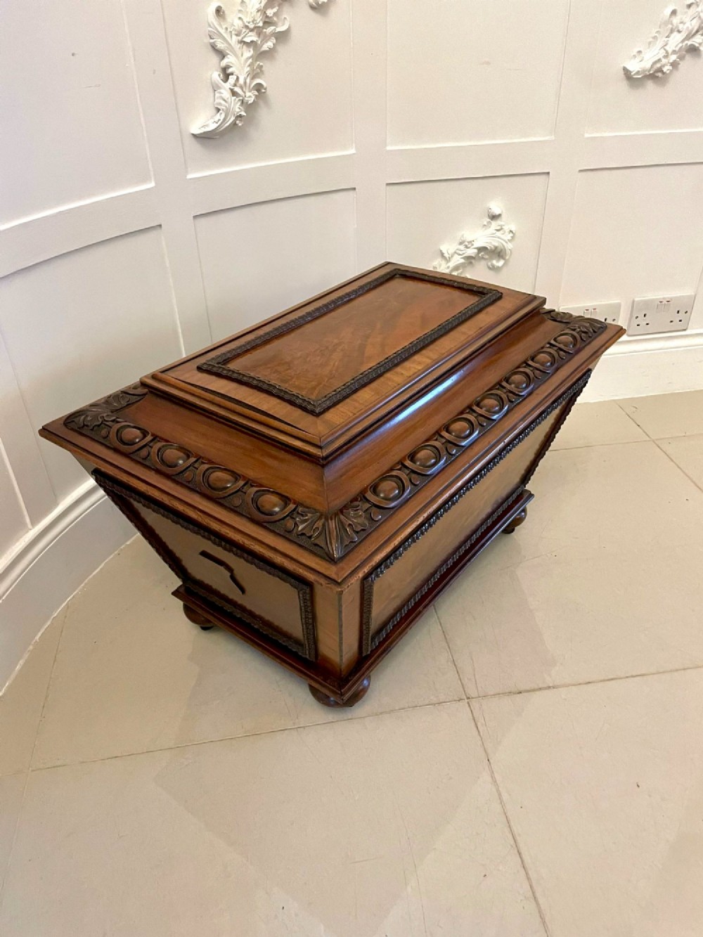 A William IV sarcophagus-shaped mahogany wine cooler featuring carved egg-and-dart moulding and a stepped lid set on short legs with castors. View X