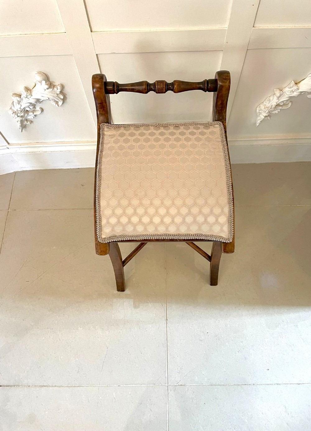 An antique Victorian wooden music chair featuring curved side supports, a turned back rail, splayed legs connected by a central stretcher, and a cream geometric upholstered seat. View IV