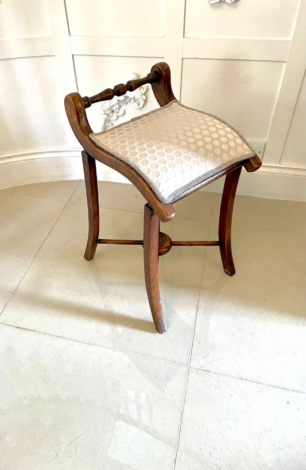 An antique Victorian wooden music chair featuring curved side supports, a turned back rail, splayed legs connected by a central stretcher, and a cream geometric upholstered seat. View V