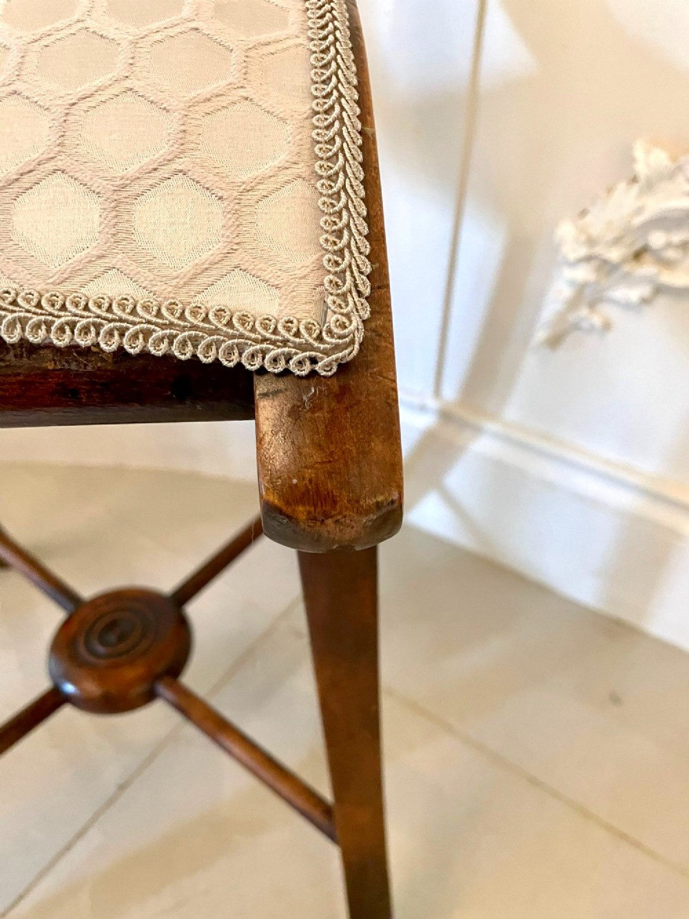An antique Victorian wooden music chair featuring curved side supports, a turned back rail, splayed legs connected by a central stretcher, and a cream geometric upholstered seat. View XII