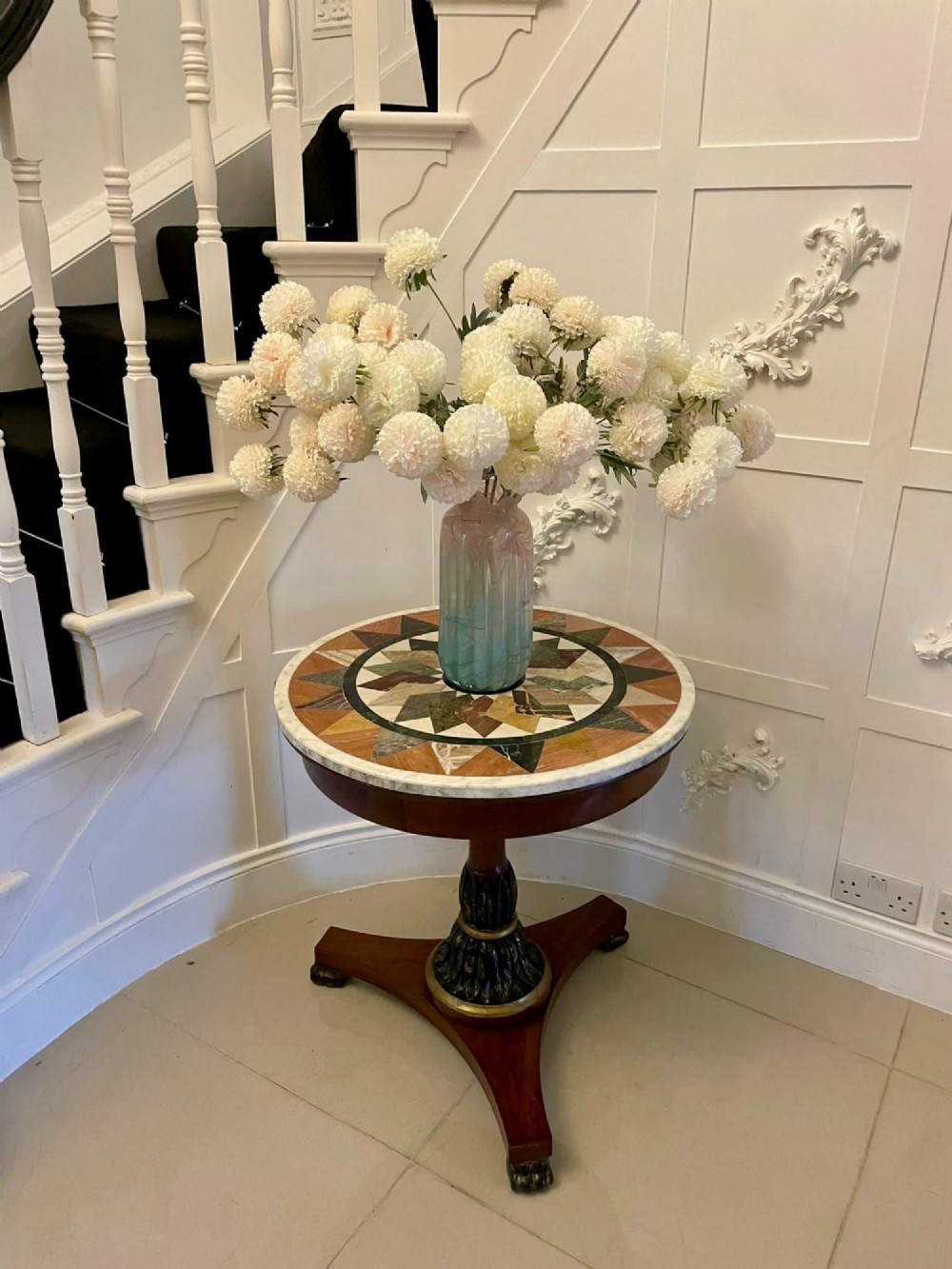 A circular Victorian centre table featuring a geometric specimen marble inlaid top resting on a dark carved mahogany pedestal with a triform base. View II