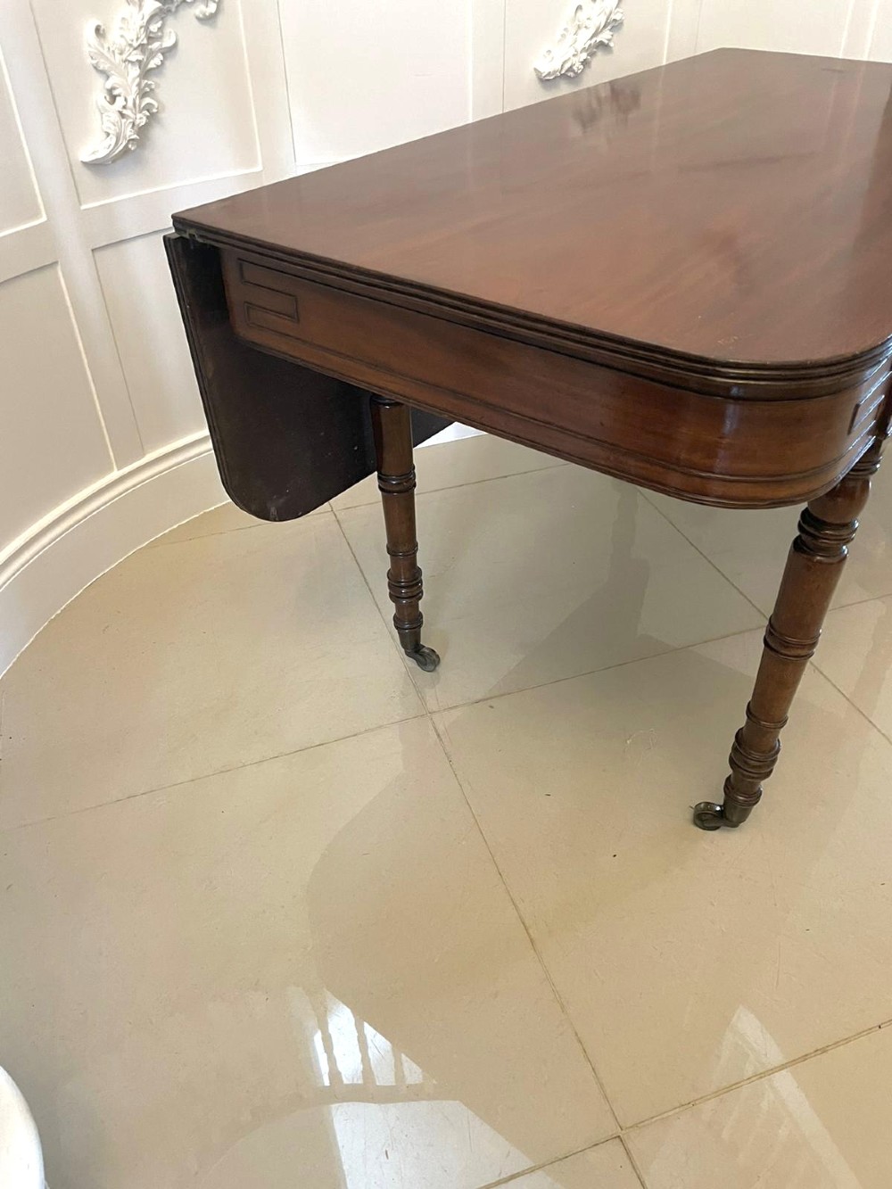 An antique George III mahogany console table featuring a polished rectangular top with rounded corners, a panelled frieze, and turned legs on brass castors. View III