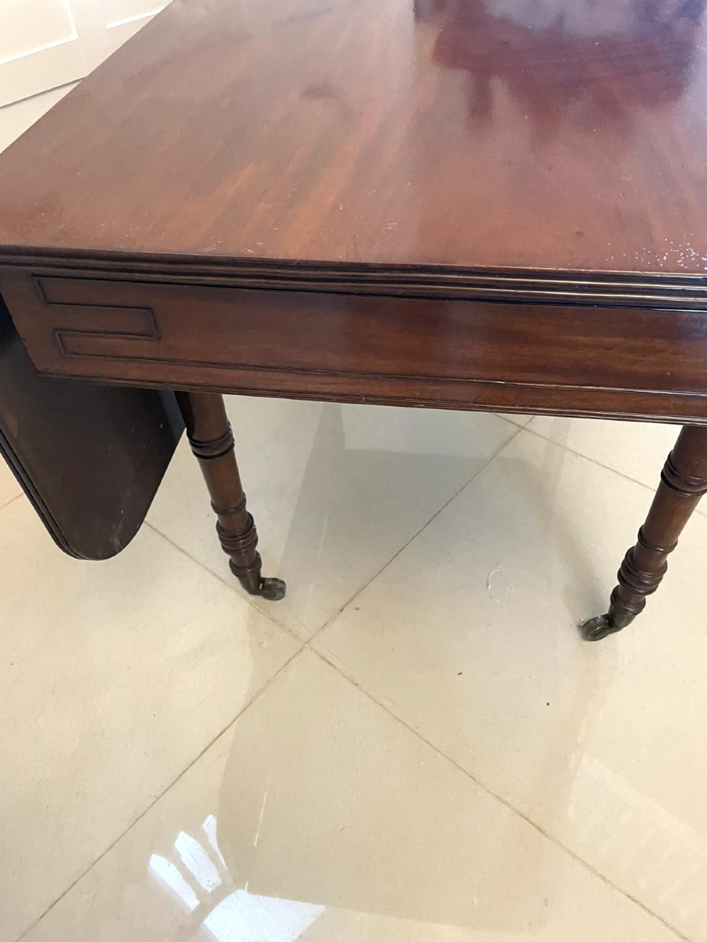 An antique George III mahogany console table featuring a polished rectangular top with rounded corners, a panelled frieze, and turned legs on brass castors. View IV