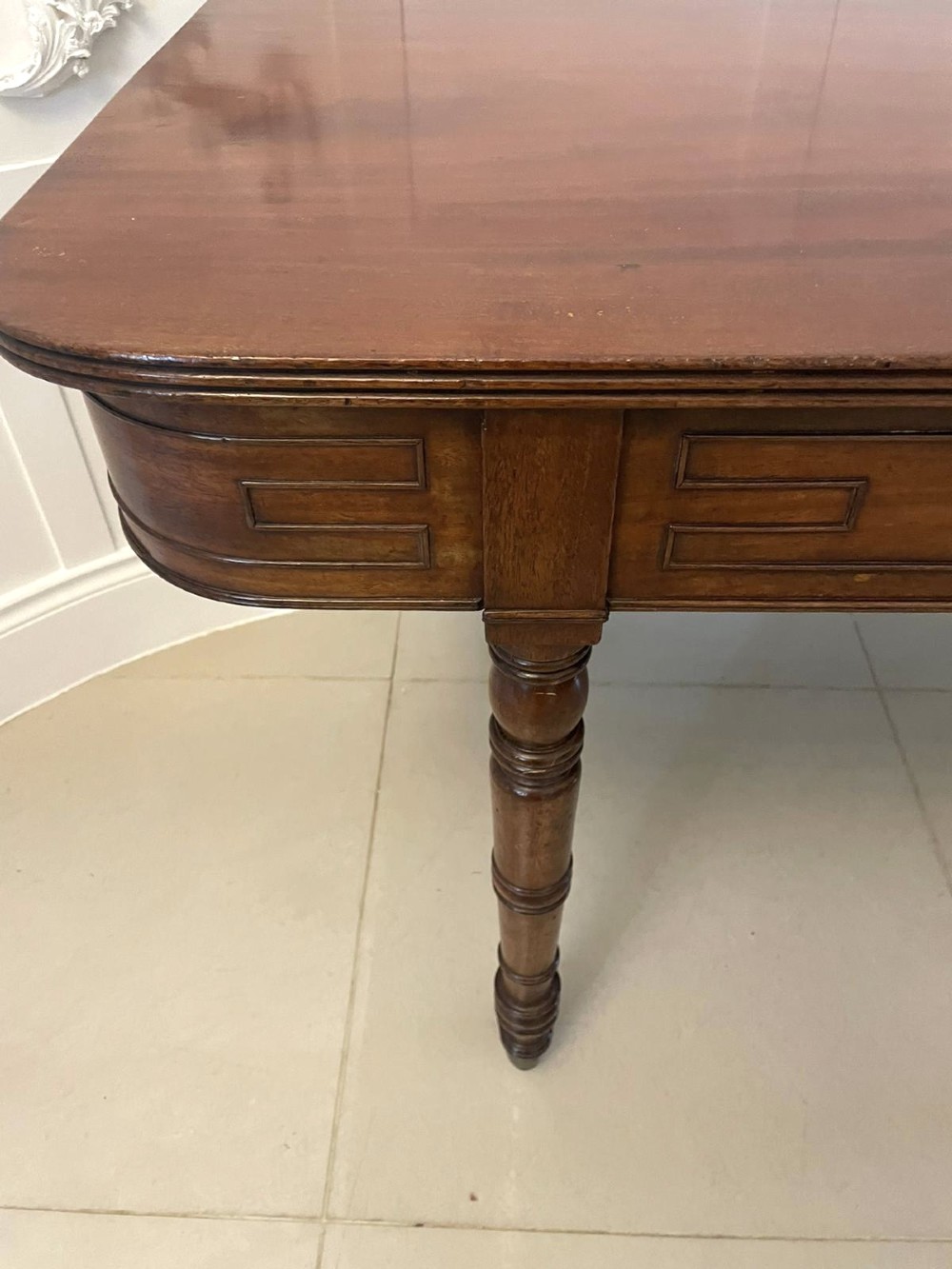 An antique George III mahogany console table featuring a polished rectangular top with rounded corners, a panelled frieze, and turned legs on brass castors. View VI