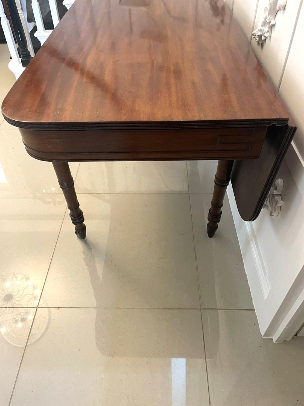 An antique George III mahogany console table featuring a polished rectangular top with rounded corners, a panelled frieze, and turned legs on brass castors. View IX