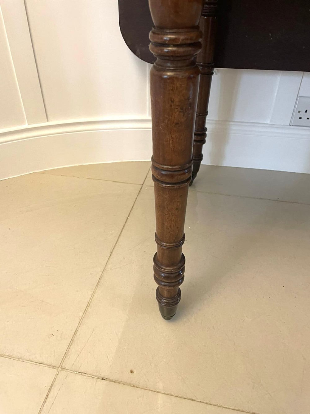 An antique George III mahogany console table featuring a polished rectangular top with rounded corners, a panelled frieze, and turned legs on brass castors. View X
