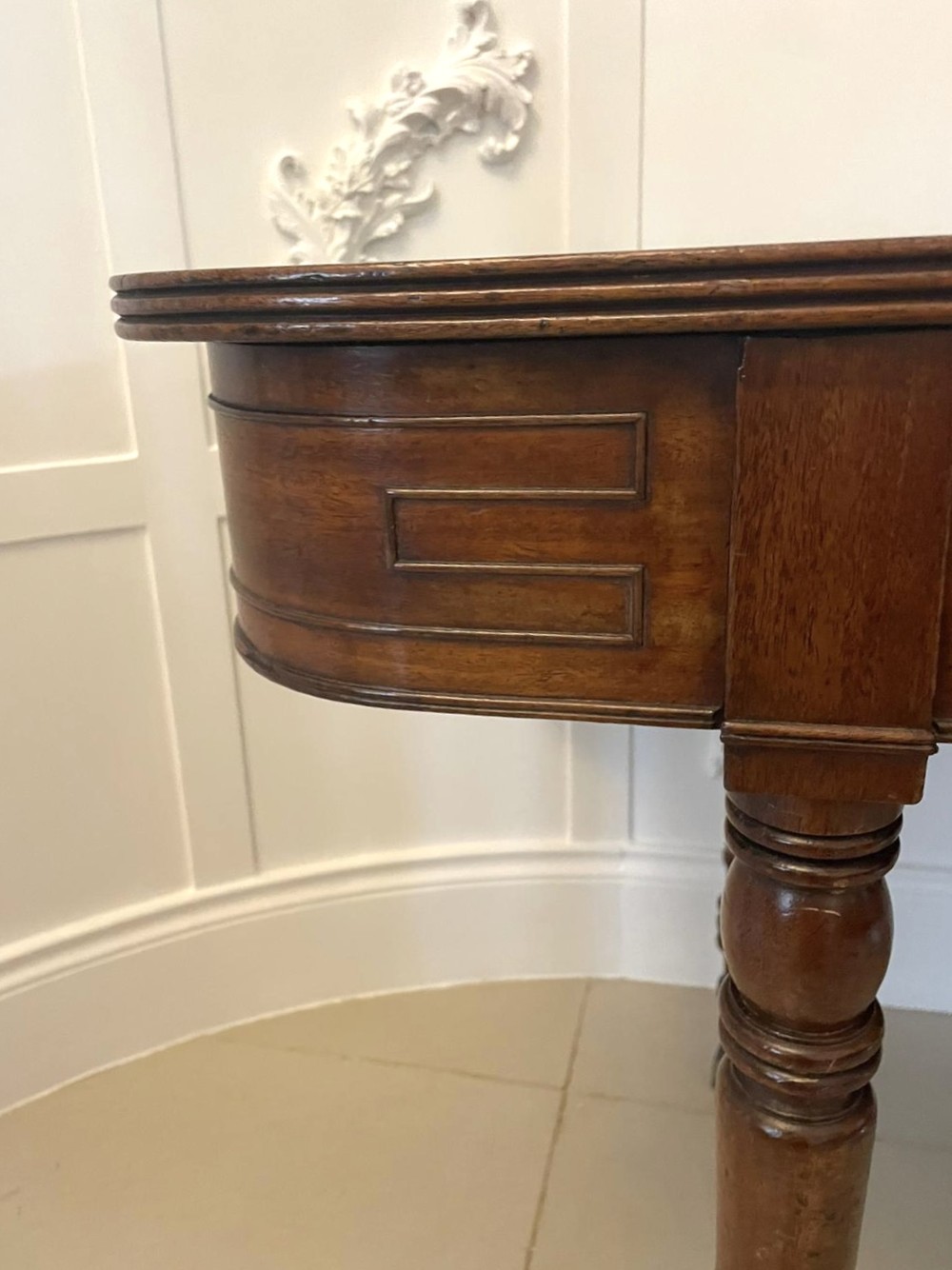 An antique George III mahogany console table featuring a polished rectangular top with rounded corners, a panelled frieze, and turned legs on brass castors. View XI